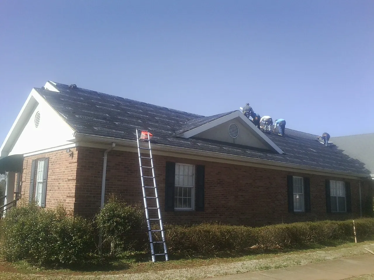 Crew tearing shingles off a brick ranch roof with a ladder set — Emergency Roof Repair work by our crew in Jacksonville