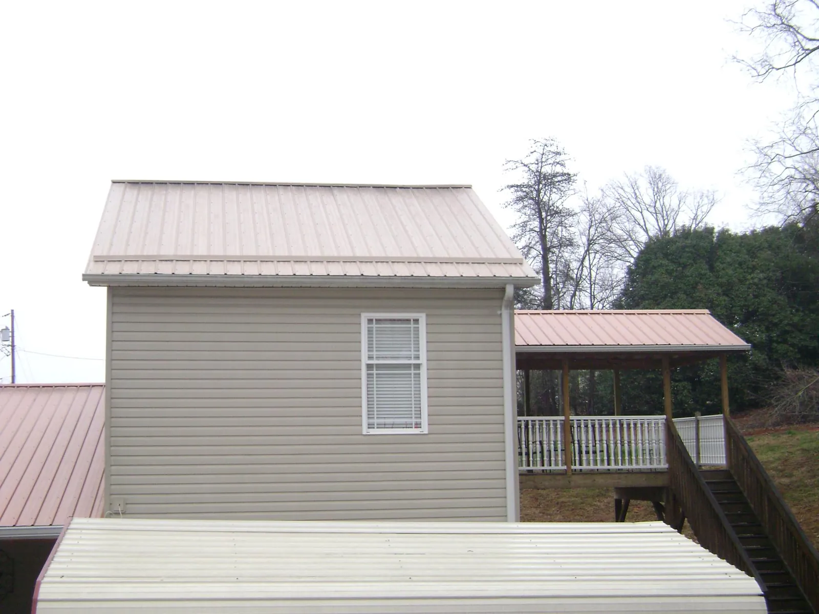 Tan metal roofs on a two story addition and attached porch, from a Roof Replacement job in Jacksonville